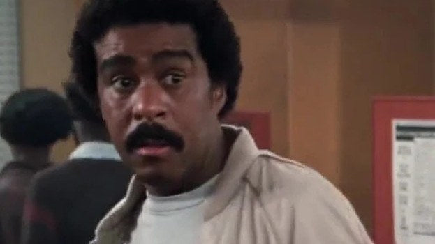 Richard Pryor como Gus Gorman, cazadora beige y camiseta blanca, en Superman III
